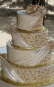 Candlelight buttercream iced,  4 tier round wedding cake decorated with Pearlescent Fondant Drapes, Gold Piped scrolls, and Gumpaste flowers. (This cake can serve receptions with 180-325 expected guests)